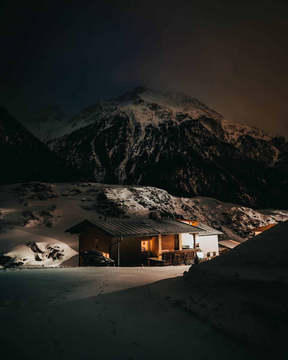 brown wooden house on snow covered ground near snow covered mountain during daytime